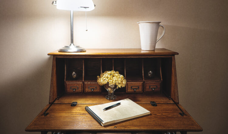 a beautiful wooden writing desk with a lamp and flowers