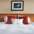 an arrangement of white and orange pillows on a clean white bed at the Smuggler’s Cove Inn.