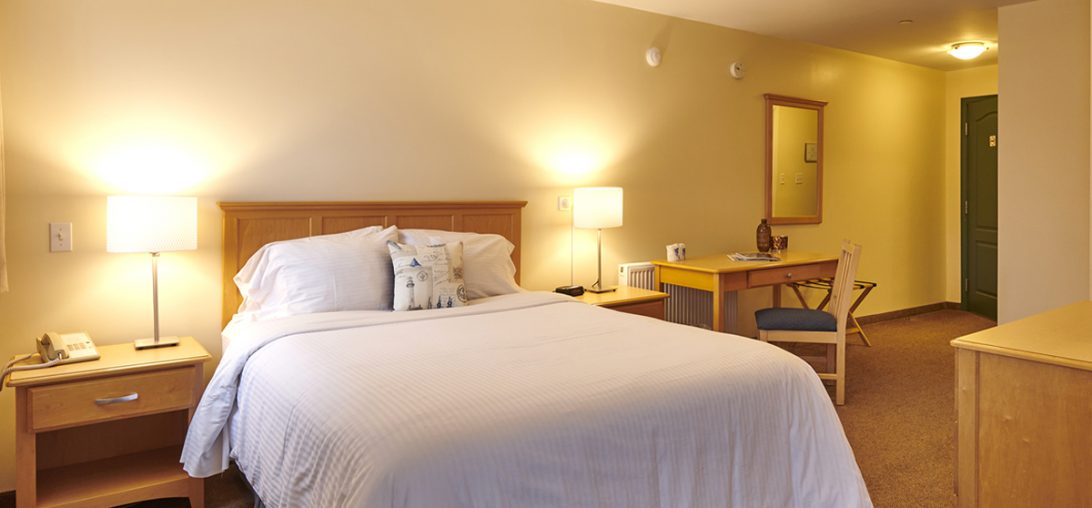 Queen sized bed and two side tables with lamps and a wooden back board in room 303.